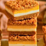 A stack of three Pumpkin Cheesecake Bars showing the Biscoff crust, cheesecake layers, and walnut crumble topping.