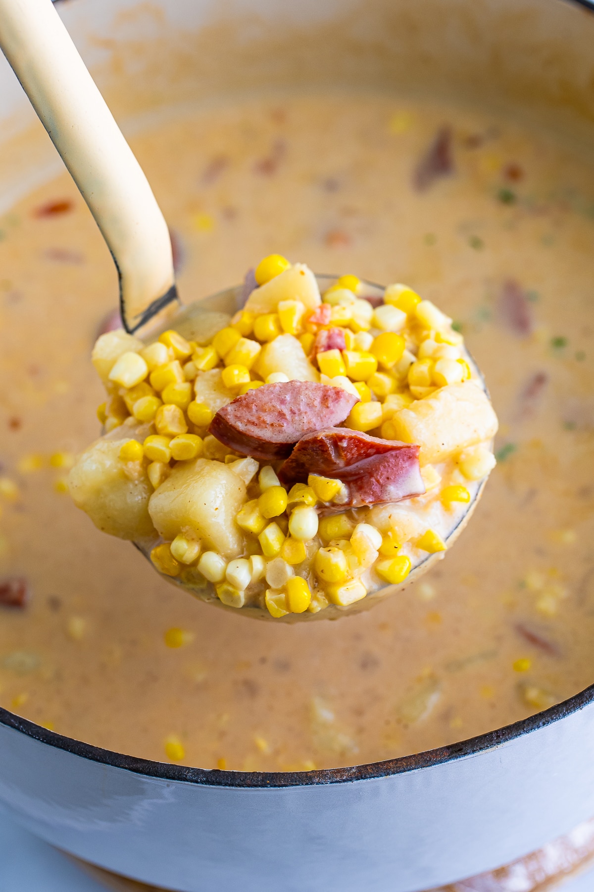 a serving spoon holding up a portion of Corn Chowder recipe over the Dutch oven