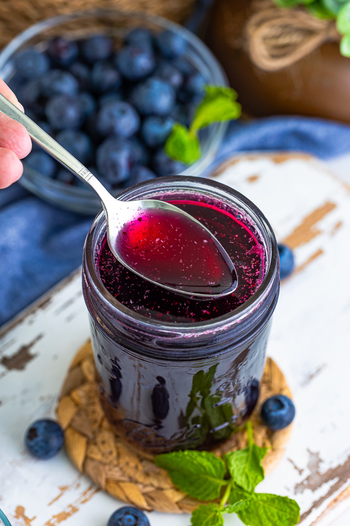 a spoon holding up Blueberry Syrup in air over a mason jar