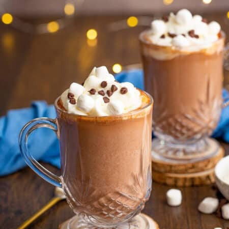 Glass mug of boozy hot chocolate topped with whipped cream, mini marshmallows, and chocolate chips.