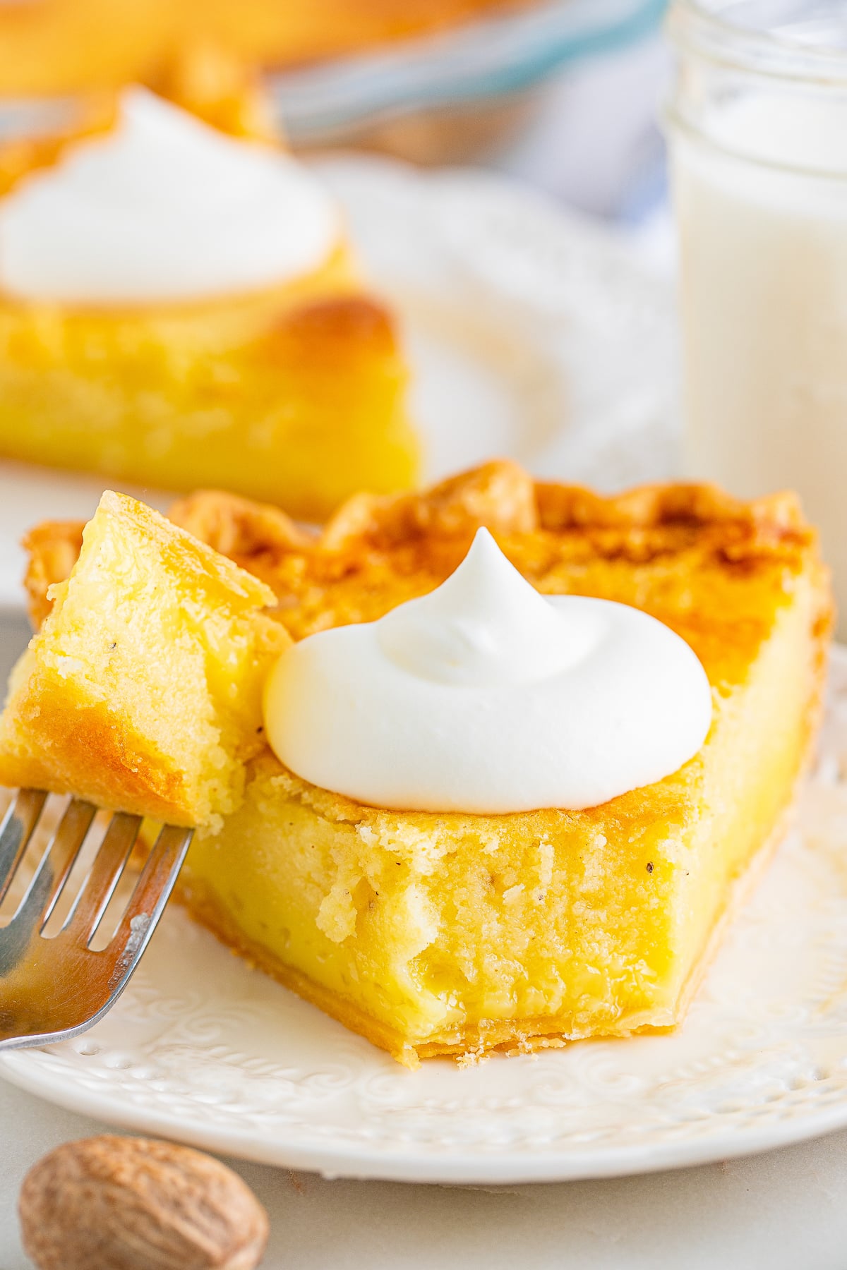 a slice of Buttermilk Pie on a white plate, close up image with a bite taken out