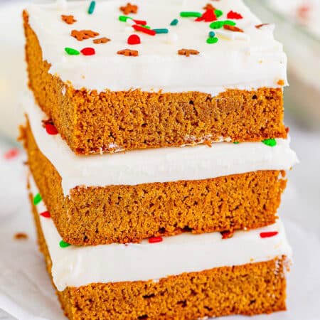 Three gingerbread bars stacked tall showing the soft spiced crumb and thick cream cheese frosting.