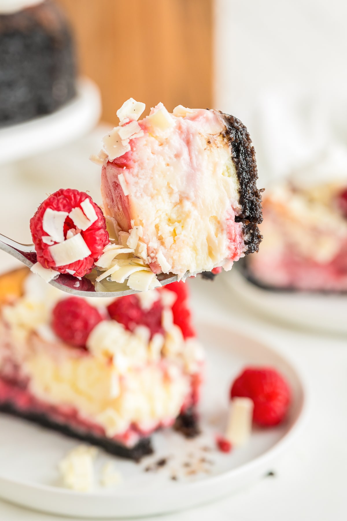 a fork holding up a bite of White Chocolate and Raspberry Cheesecake in air