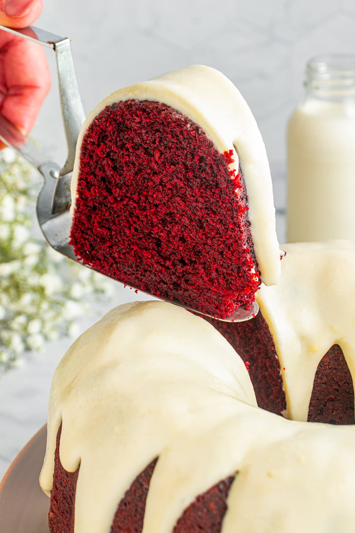 a cake server holding up a slice of Red Velvet Bundt Cake in air