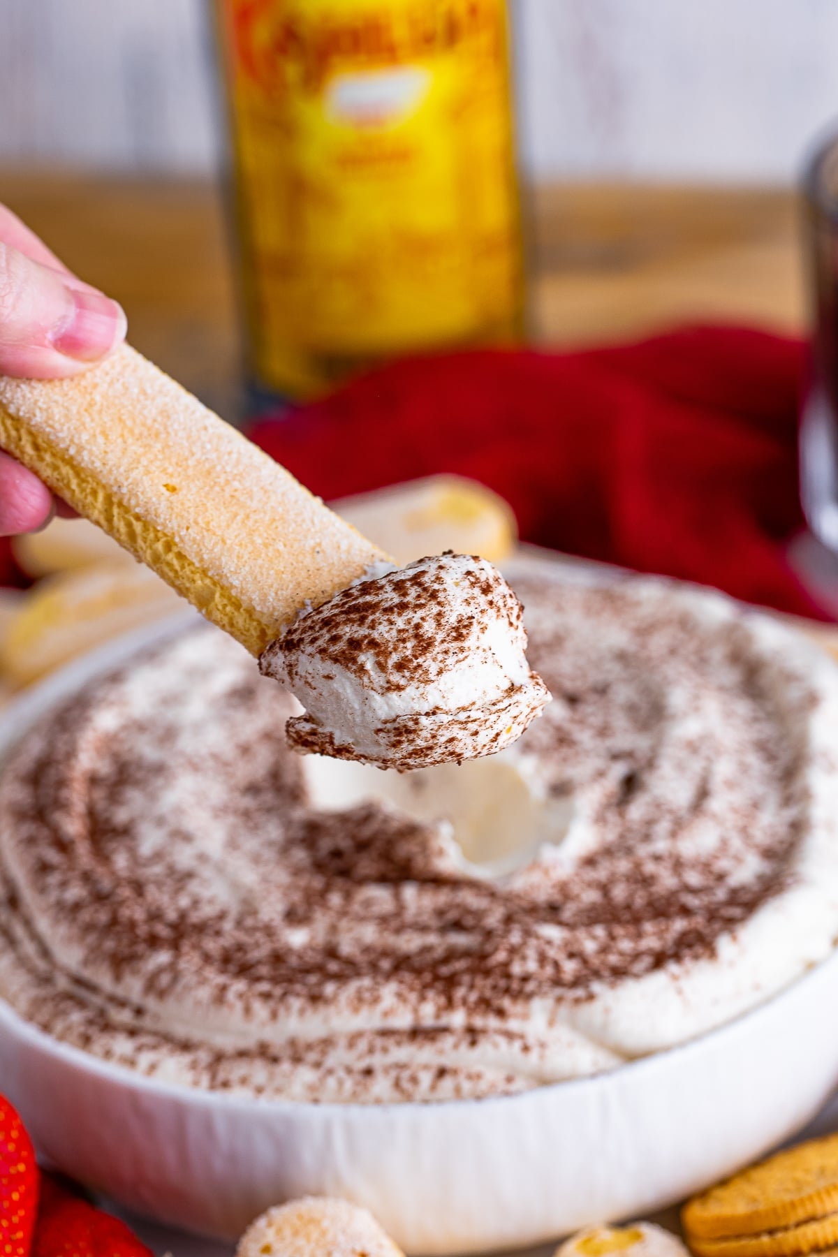 a hand holding up a lady finger in air that has Tiramisu Dip on it