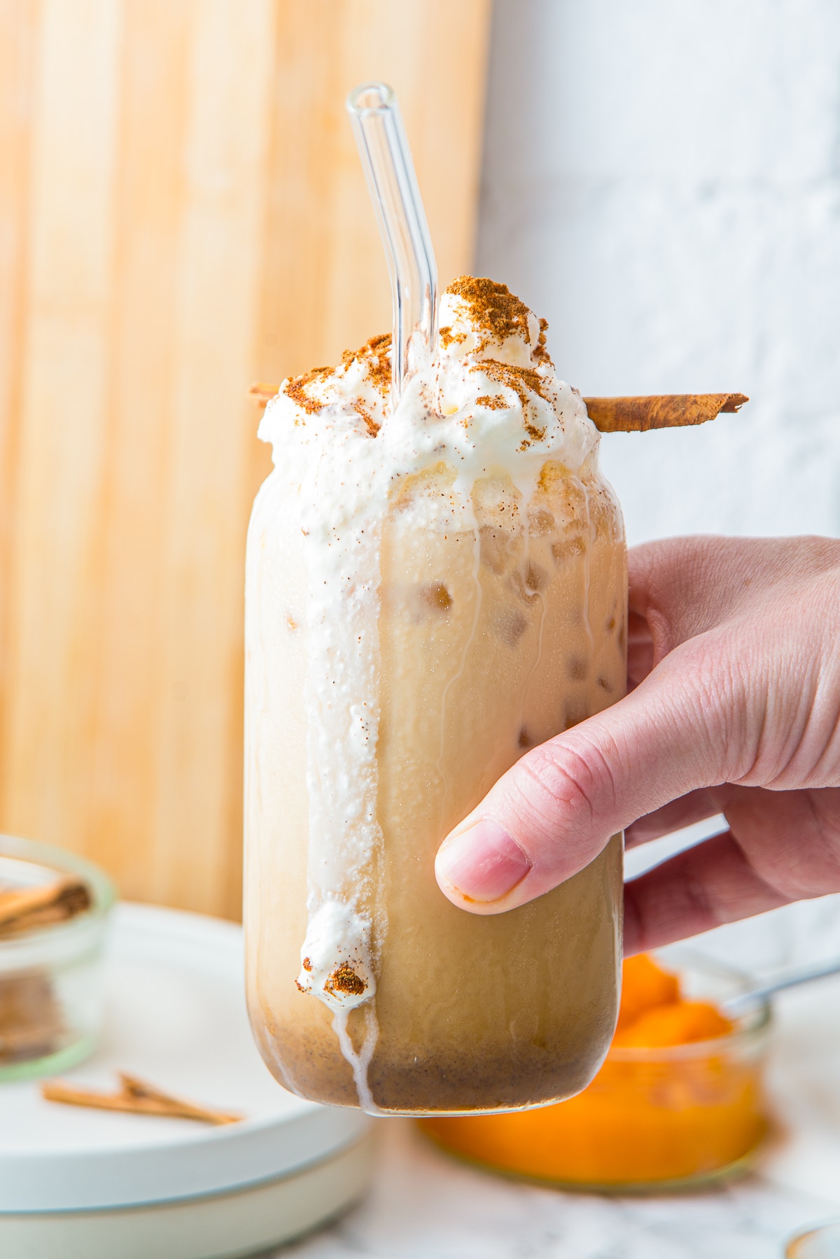 a hand holding up a Iced Pumpkin Spiced Latte in air