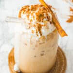 An iced pumpkin spice latte topped with whipped cream and a cinnamon stick on a marble counter.