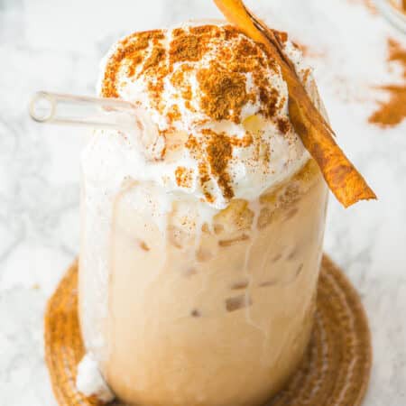 An iced pumpkin spice latte topped with whipped cream and a cinnamon stick on a marble counter.