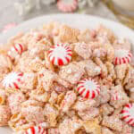 White chocolate chex mix on a white plate surrounded by starlight peppermints.