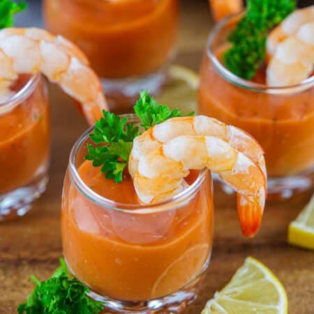 Shrimp cocktail served in individual shot glasses with cocktail sauce and parsley.