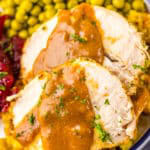 A plate of sliced slow cooker turkey breast with gravy, rice, and cranberry sauce.