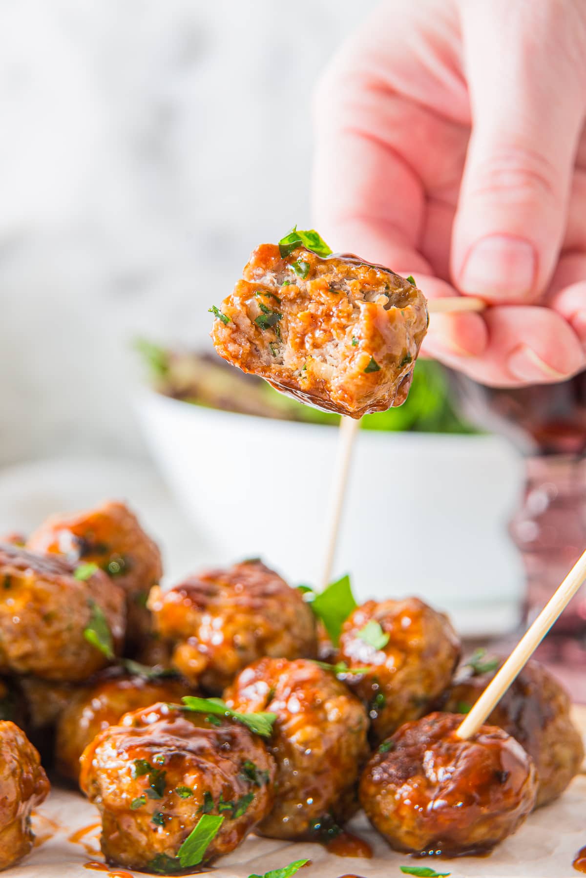a hand holding up a toothpick with BBQ meatballs on it with a bite taken out