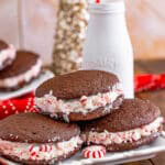 A plate of chocolate Whoopie Pies with fluffy marshmallow filling rolled in crushed peppermints, milk bottle behind.