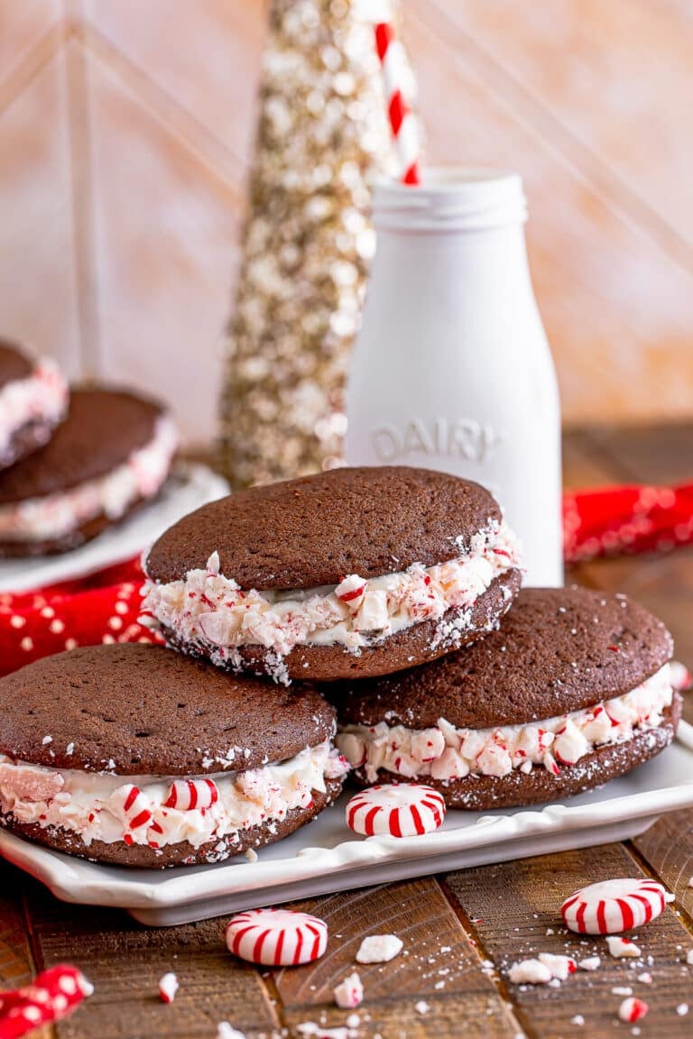 A plate of chocolate Whoopie Pies with fluffy marshmallow filling rolled in crushed peppermints, milk bottle behind.