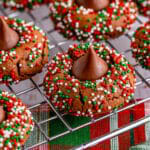 Chocolate blossom cookies rolled in red and green nonpareils with chocolate kisses pressed in the centers, cooling on a wire rack.