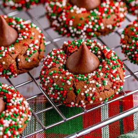 Chocolate blossom cookies rolled in red and green nonpareils with chocolate kisses pressed in the centers, cooling on a wire rack.