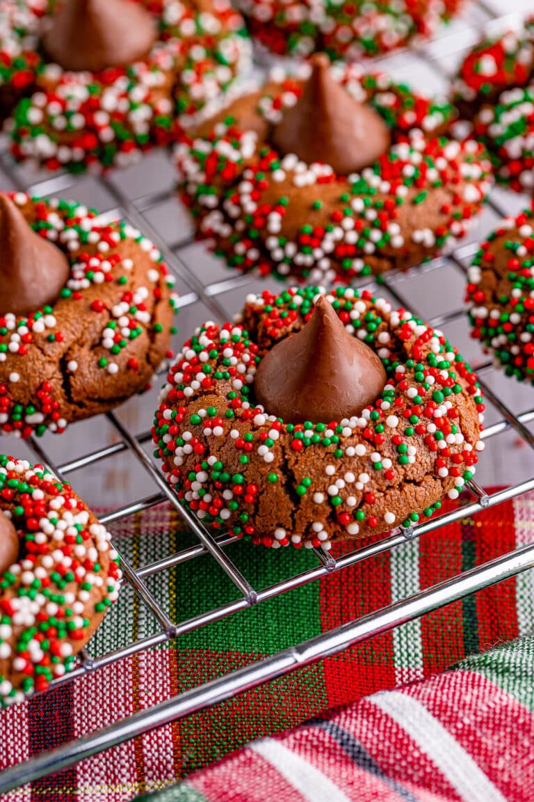 Chocolate blossom cookies rolled in red and green nonpareils with chocolate kisses pressed in the centers, cooling on a wire rack.