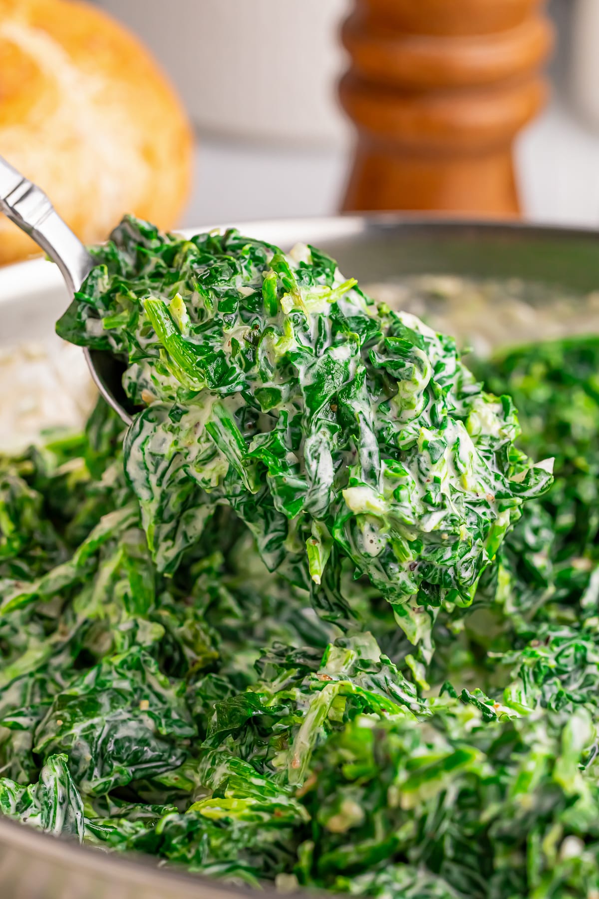 a spoon holding up a helping of Creamed Spinach in the air