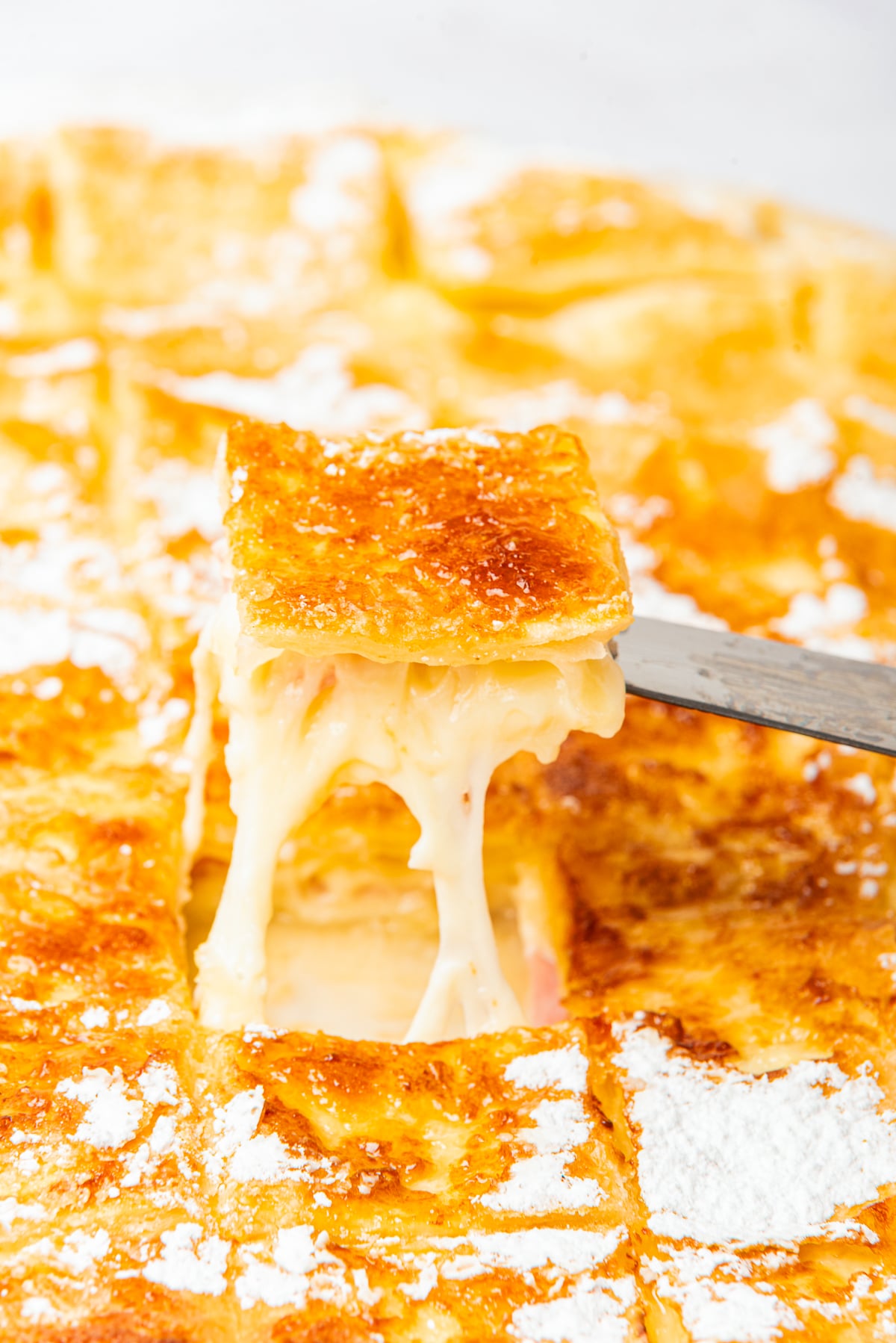 a spatula holding up Ham Squares in air with cheese pull