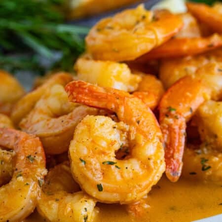 A plate of New Orleans BBQ shrimp in a rich buttery sauce served with crusty bread.
