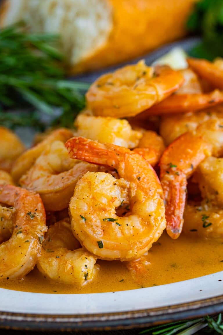 A plate of New Orleans BBQ shrimp in a rich buttery sauce served with crusty bread.