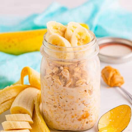 A mason jar of peanut butter overnight oats topped with banana slices and a spoon.