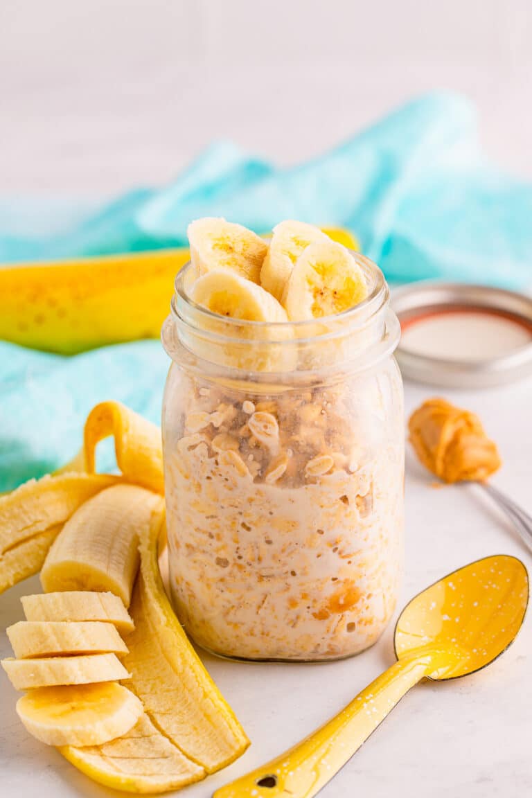 A mason jar of peanut butter overnight oats topped with banana slices and a spoon.
