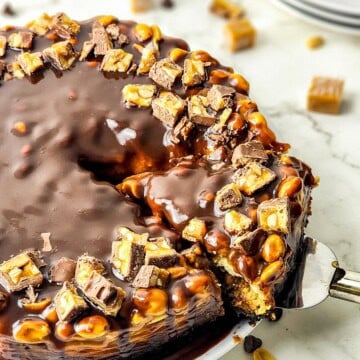A whole Snickers cheesecake with chocolate ganache drip and Snickers chunks on top.