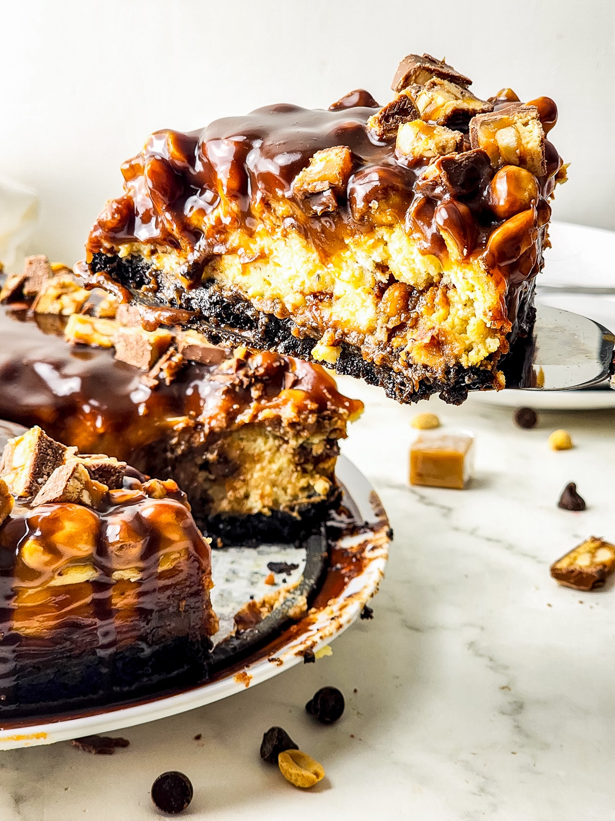 a cake server holding up a slice of Snickers Cheesecake in air