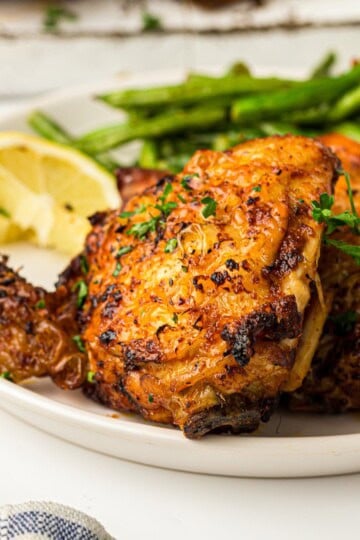 Crispy golden air fryer chicken thighs plated with roasted asparagus and a lemon wedge.