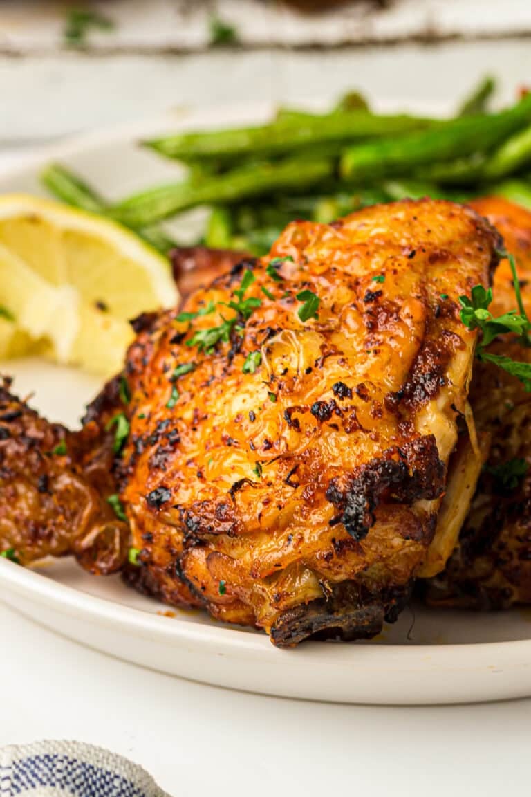 Crispy golden air fryer chicken thighs plated with roasted asparagus and a lemon wedge.