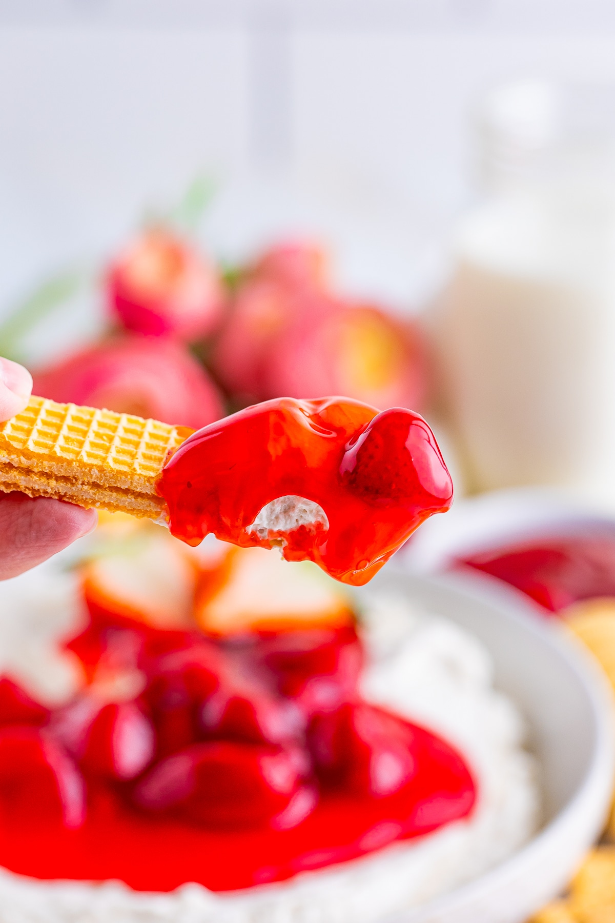 a hand holding up a cookie with Cheesecake Dip on it in air