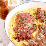 Steak Alfredo in a skillet with sliced ribeye over creamy fettuccine garnished with Parmesan and parsley.
