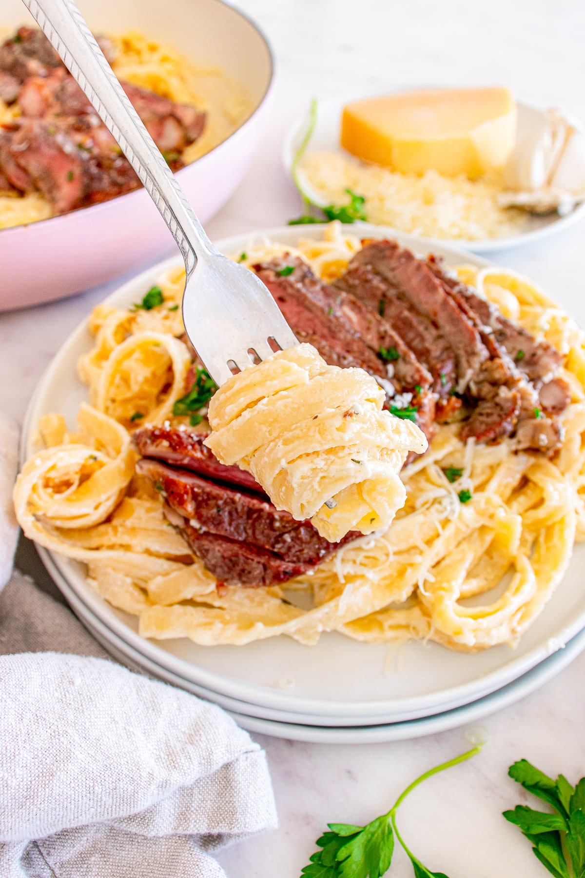 a fork holding up a bite of Steak Pasta Alfredo in air