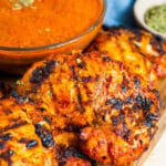 Grilled chipotle chicken thighs on a wooden board next to a bowl of chipotle chicken marinade.