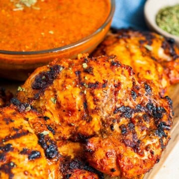 Grilled chipotle chicken thighs on a wooden board next to a bowl of chipotle chicken marinade.