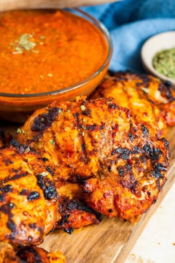 Grilled chipotle chicken thighs on a wooden board next to a bowl of chipotle chicken marinade.