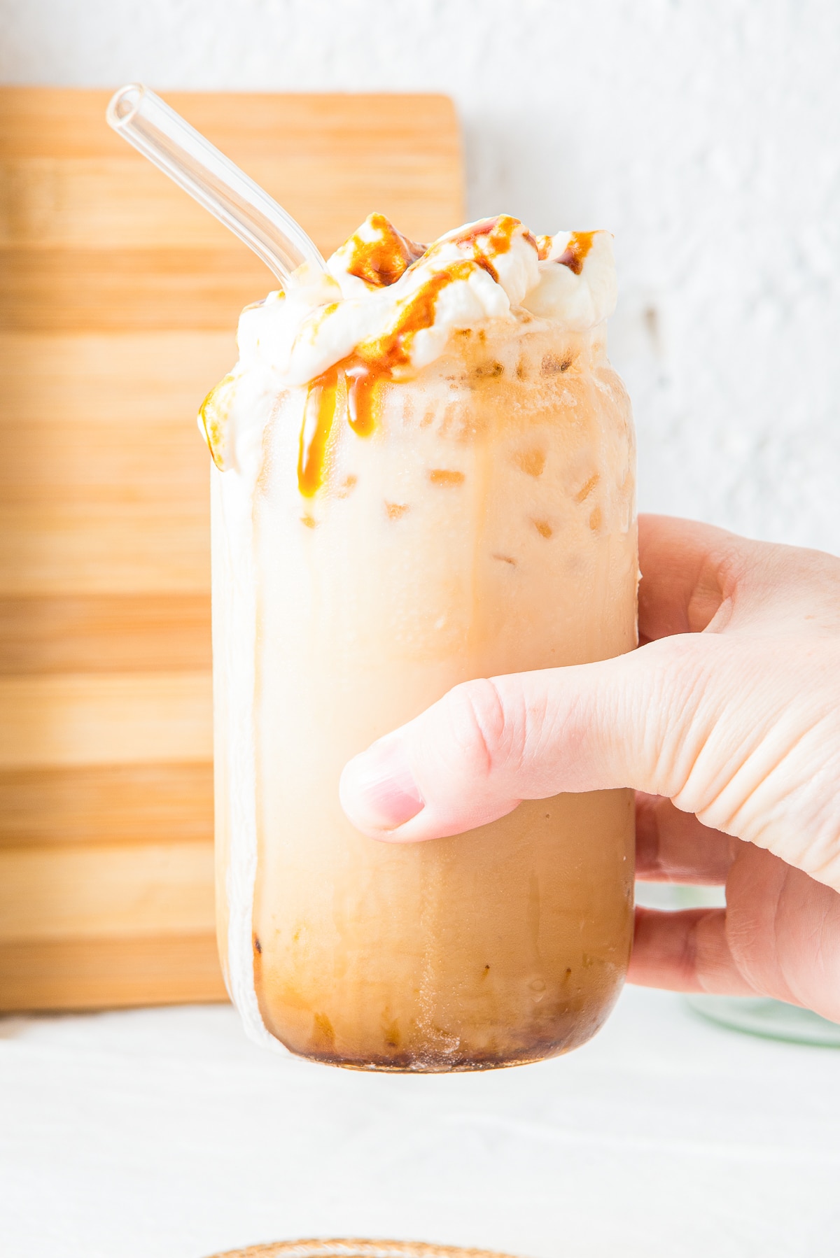 a hand holding up Iced Caramel Latte in air