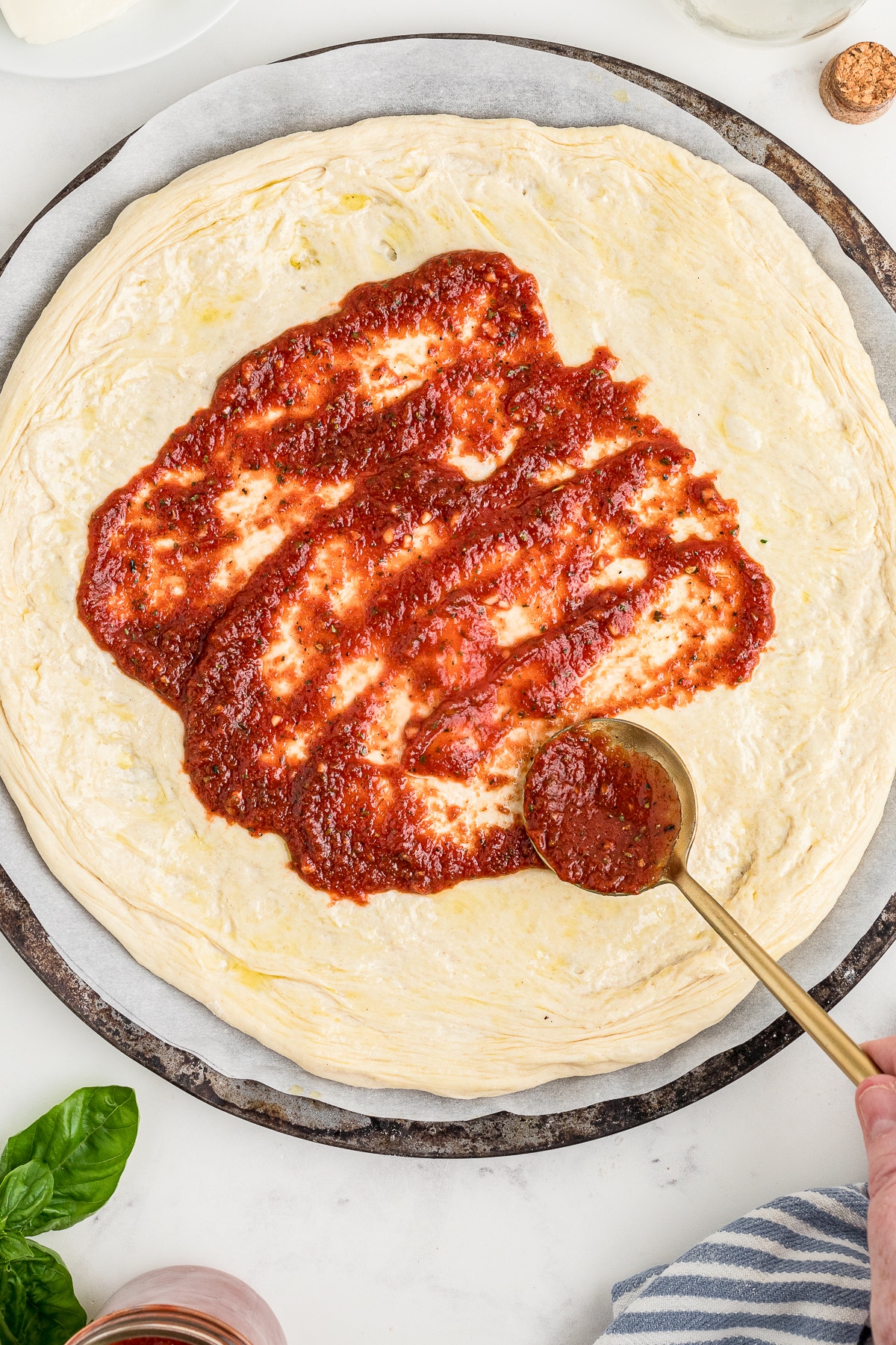 a spoon spreading Pizza Sauce on pizza dough