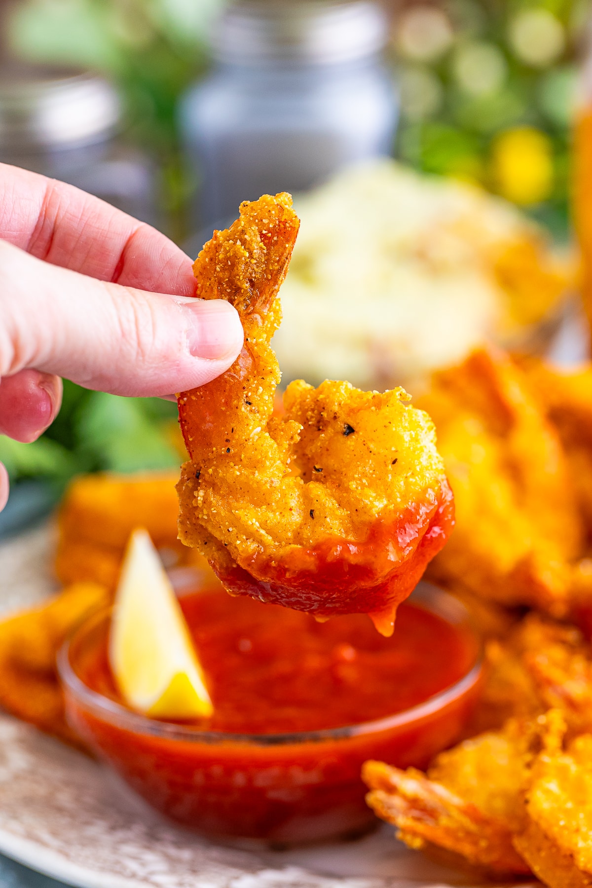 a hand holding up a Fried Shrimp in air that has been dipped in cocktail sauce