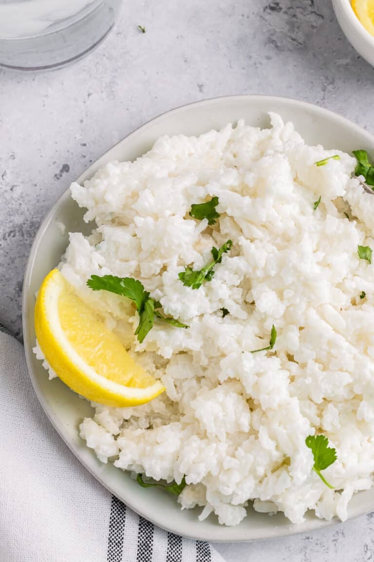 A bowl of fluffy coconut rice garnished with fresh cilantro and a lemon wedge