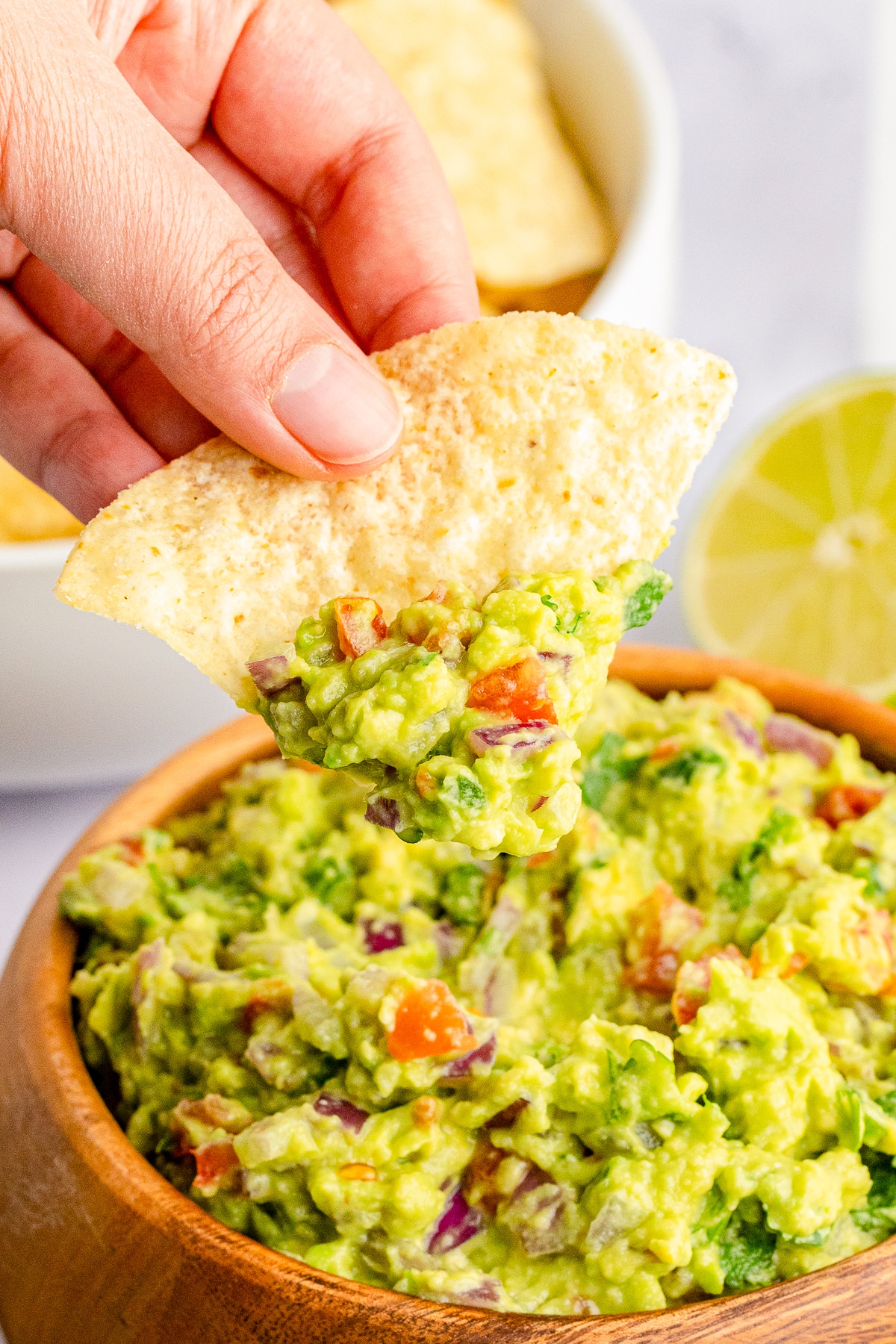 a hand holding up a chip that has guacamole on it