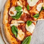 A whole margherita pizza topped with fresh mozzarella and basil on a board