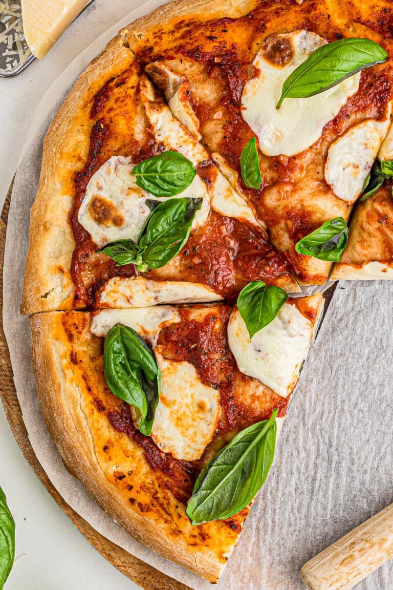 A whole margherita pizza topped with fresh mozzarella and basil on a board