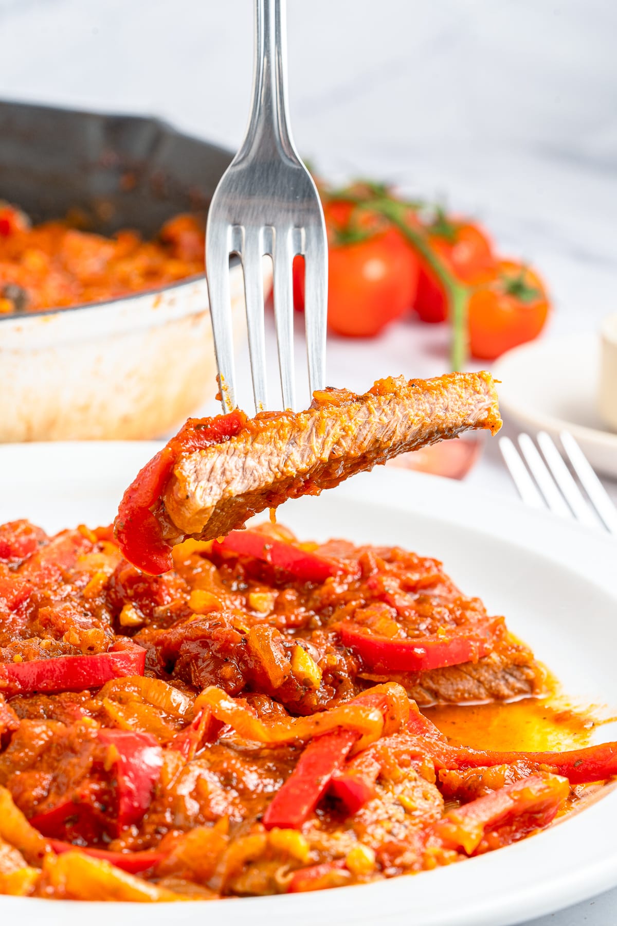 a fork holding up a bite of Steak Pizzaiola in air