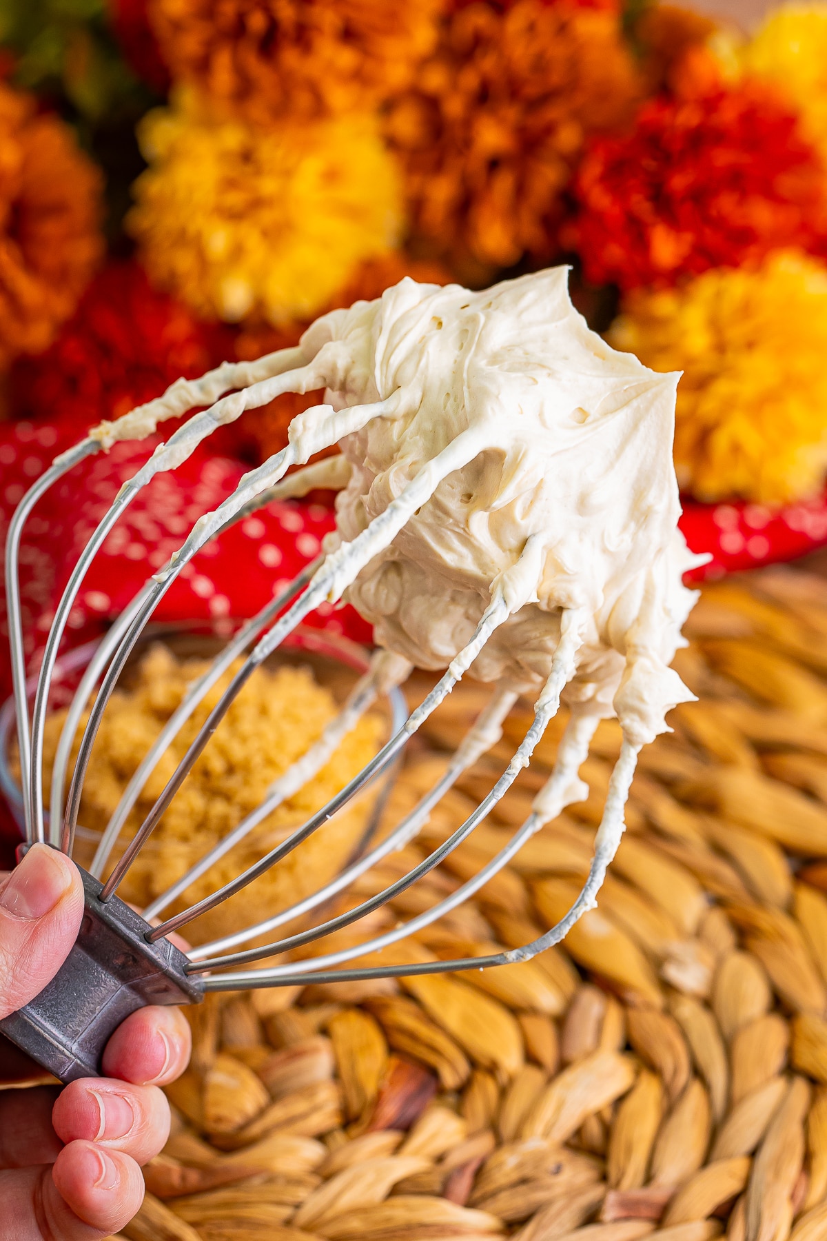 a hand holding up a whisk Brown Sugar Frosting on it