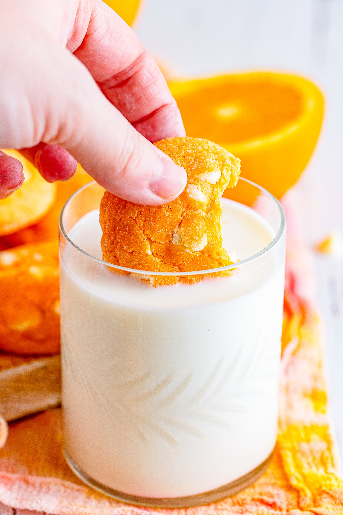 a hand dipping a Orange Creamsicle Cookies into a glass of milk