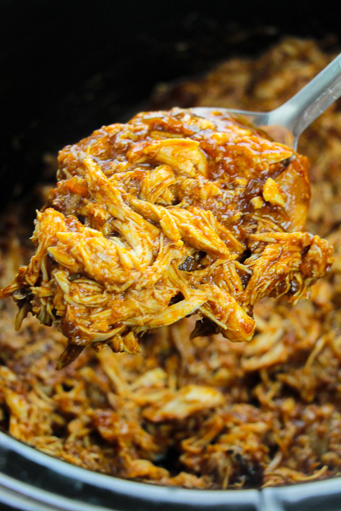 a spoon holding up Crockpot Pulled Chicken Tacos over cooker