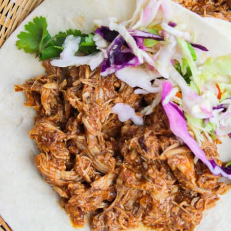 Crockpot chicken tacos on a plate topped with cabbage slaw, cilantro, and lime.