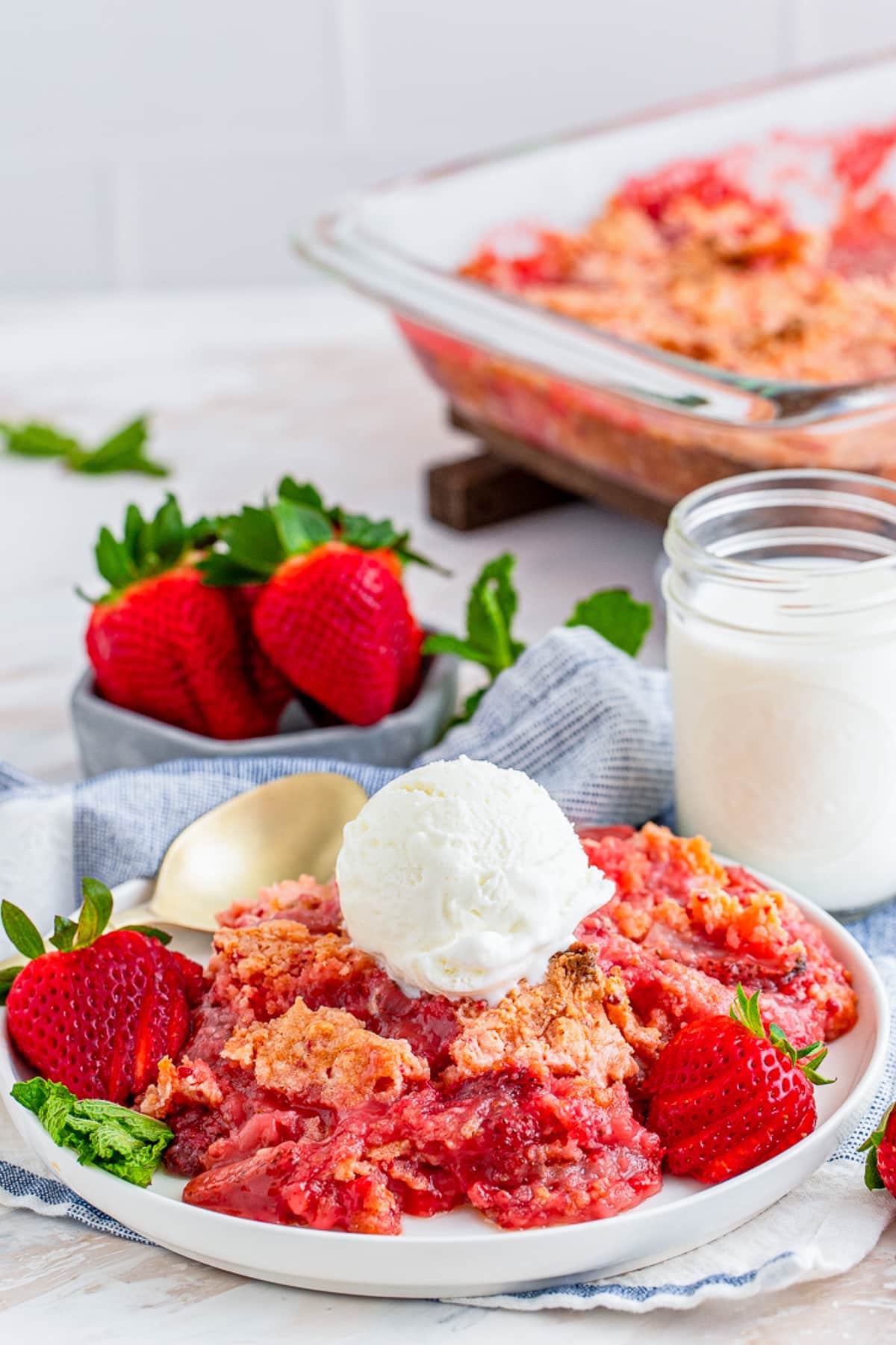 a serving of Strawberry Dump Cake on a plate with baking dish in the back